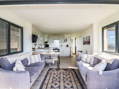 A living room with two sofas and a patterned rug next to a kitchen with dining table and chairs at Sandpiper Chalet in Eype
