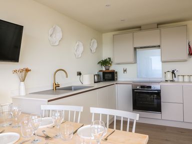 A kitchen with a dining table set with plates and glasses a gold faucet a microwave an oven and cabinets at Sandpiper Chalet in Eype
