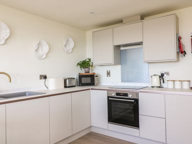 A kitchen with beige cabinets a built in oven microwave toaster kettle and wall decor at Sandpiper Chalet in Eype