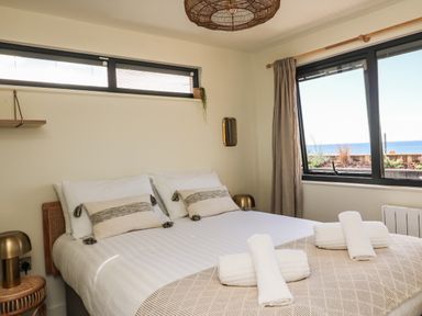 A bedroom with a bed with rolled towels on it a window with curtains and a view of the sea at Sandpiper Chalet in Eype