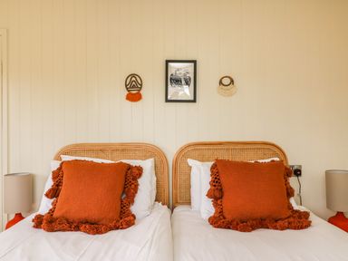 A bedroom with two beds each with a large orange cushion and wicker headboards at Sandpiper Chalet in Eype