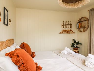 A bedroom with a double bed with orange pillows a wall rack with hangers a round shelf with books and a potted plant at Sandpiper Chalet in Eype