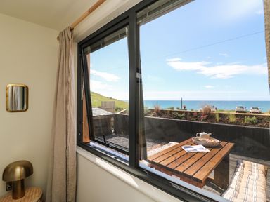 A window view showing a wooden outdoor table with tea set and cushions overlooking the sea at Sandpiper Chalet in Eype