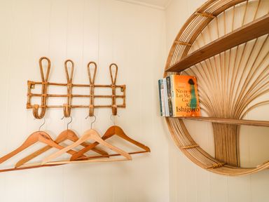 A wall with wooden coat hangers on hooks and a circular wooden shelf holding books at Sandpiper Chalet in Eype