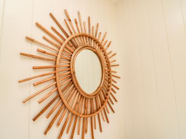 A round mirror with a sunburst wooden frame hanging on a beige paneled wall at Sandpiper Chalet in Eype