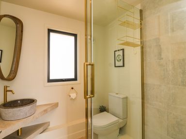 A bathroom with a stone sink and gold faucet a wall mirror a toilet and a glass shower enclosure at Sandpiper Chalet in Eype