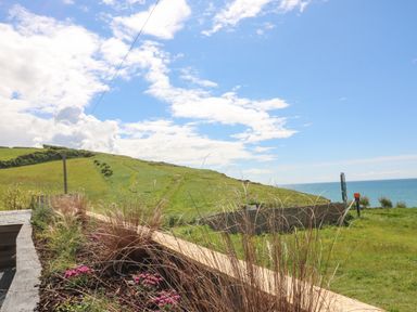 A grassy hillside with a pathway near the sea under a partly cloudy sky