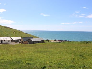 A grassy field with houses near a coastline and parked cars by the sea at Sandpiper Chalet in Eype