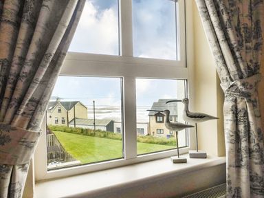 A window with curtains and bird sculptures on the sill overlooking houses and a grassy area at Beach View in Duncannon near Ramsgrange County Wexford