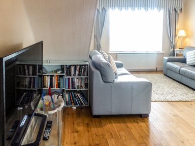 A living room with two sofas a TV on a stand a bookshelf and a window with striped curtains at Beach View in Duncannon near Ramsgrange County Wexford
