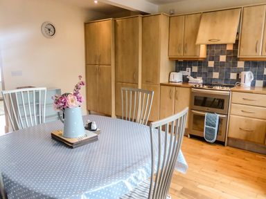 A kitchen with wooden cabinets a gas stove dining table with a polka dot tablecloth and flowers in a jug at Beach View in Duncannon near Ramsgrange County Wexford