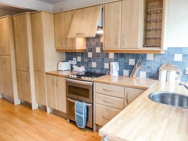 A kitchen with wooden cabinets a stove a sink a kettle and a toaster at Beach View in Duncannon near Ramsgrange County Wexford