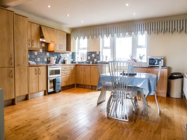 A kitchen with wooden cabinets a dining table with chairs and a blue tablecloth at Beach View in Duncannon near Ramsgrange County Wexford
