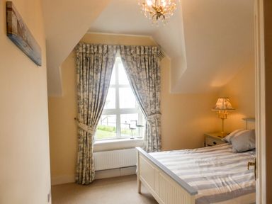 A bedroom with a bed a bedside table with a lamp a window with curtains and a painting on the wall at Beach View in Duncannon near Ramsgrange County Wexford