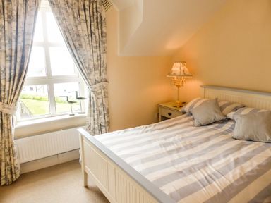 A bedroom with a bed with striped bedding a nightstand with a lamp and curtains at Beach View in Duncannon near Ramsgrange County Wexford