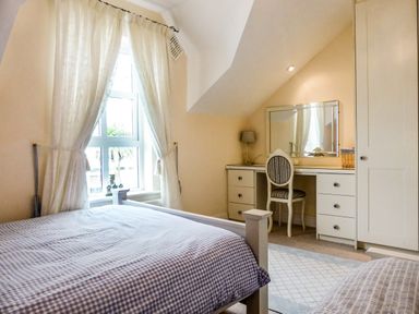 A bedroom with a bed near a window with curtains and a dressing table with a chair and a mirror at Beach View in Duncannon near Ramsgrange County Wexford