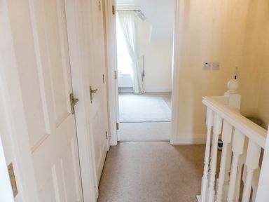 A hallway with white doors and a railing leading to a room with a window and curtains at Beach View in Duncannon near Ramsgrange County Wexford