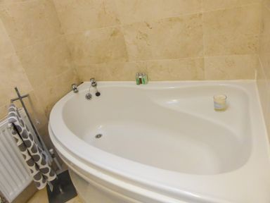 A corner bathtub with a candle and toiletries in a beige tiled bathroom at Beach View in Duncannon near Ramsgrange County Wexford