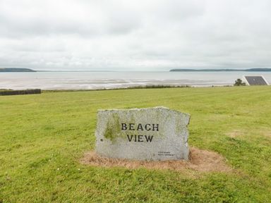 A stone sign reading Beach View on a grassy area with a beach and water in the background at Beach View in Duncannon near Ramsgrange County Wexford