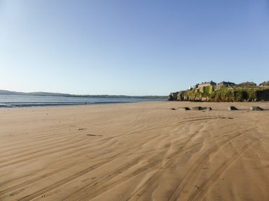 A sandy beach with tire tracks and footprints near water and rocky cliffs with buildings at Beach View in Duncannon near Ramsgrange County Wexford