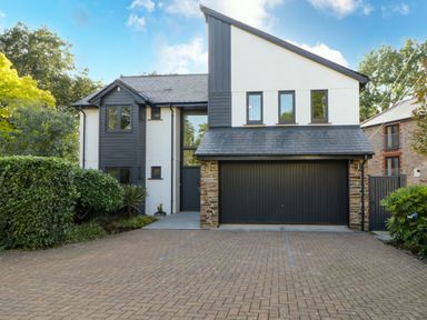 A modern two-story house with a large garage door and driveway surrounded by greenery at Iroko in Millbrook
