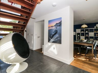 A hallway with a modern round chair and wooden staircase leading up with a dining room in the background at Iroko Millbrook