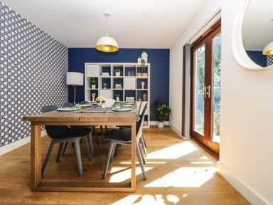 A dining room with a wooden table set for six and a white shelving unit against a blue wall with a patterned wall at Iroko in Millbrook