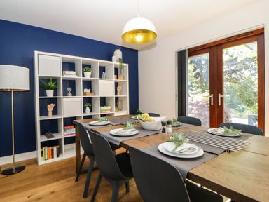 A dining room with a wooden table set for six next to a white shelving unit and glass doors at Iroko in Millbrook