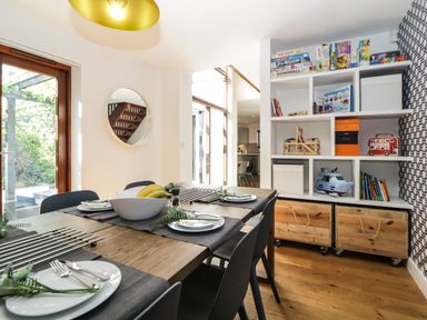 A dining area with a wooden table set with plates and cutlery near shelves with toys and books at Iroko in Millbrook