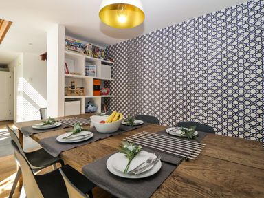 A dining table set with plates and cutlery in a room with patterned wallpaper and shelves with board games at Iroko in Millbrook