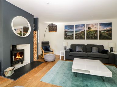 A living room with a fireplace a dark gray sofa a white coffee table and landscape pictures on the wall at Iroko in Millbrook
