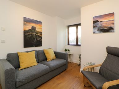 A sitting area with a grey sofa with yellow cushions a grey armchair and two landscape paintings on the walls at Iroko in Millbrook