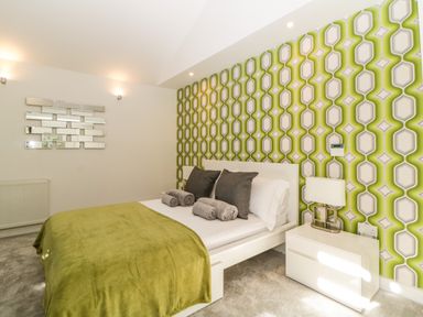 A bedroom with a white bed green and white patterned wallpaper and a white bedside table with a lamp at Iroko in Millbrook
