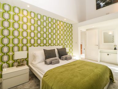 A bedroom with a bed with green blanket and patterned wallpaper at Iroko in Millbrook