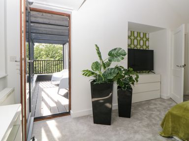 A bedroom with two black plant pots near a door leading to a balcony with white chairs at Iroko in Millbrook