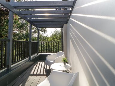 A balcony with two white chairs a round table with a plant and wooden railing at Iroko in Millbrook