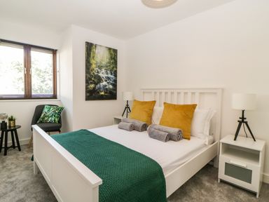 A bedroom with a white bed with green and yellow bedding a chair and a side table with a lamp at Iroko in Millbrook