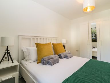 A bedroom with a bed with yellow pillows and rolled towels bedside tables with lamps and a wardrobe with a mirrored door at Iroko in Millbrook
