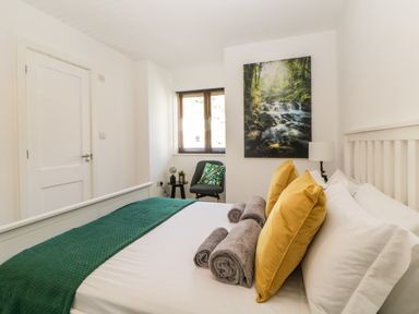 A bedroom with a neatly made bed with yellow pillows and rolled towels next to a window with a chair and a wall picture at Iroko in Millbrook
