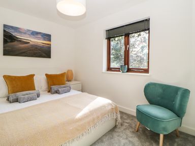 A bedroom with a bed with mustard pillows and gray towels a green chair and a window at Iroko in Millbrook