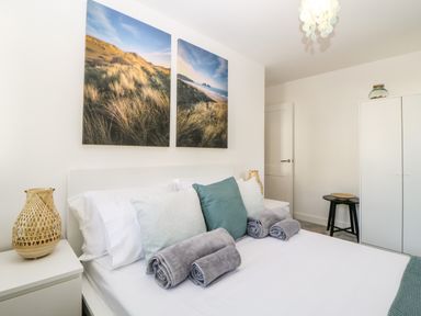 A bedroom with a bed with rolled towels and pillows two landscape paintings on the wall bedside tables with lamps a wardrobe and a stool at Iroko Millbrook