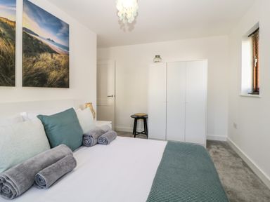 A bedroom with a bed with pillows and rolled towels a white wardrobe a window and a small stool at Iroko in Millbrook