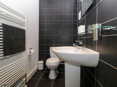 A bathroom with a white toilet and white sink with black tiled walls and a white towel rail with a dark towel at Iroko in Millbrook