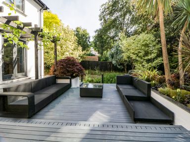 An outdoor patio with black wicker sofas and a glass-top table surrounded by trees and plants at Iroko in Millbrook