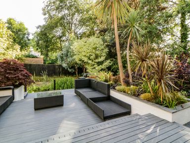 An outdoor patio with black wicker seating and a coffee table surrounded by trees and plants at Iroko in Millbrook
