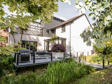 A house with a wooden deck patio and grill surrounded by trees and plants at Iroko Millbrook