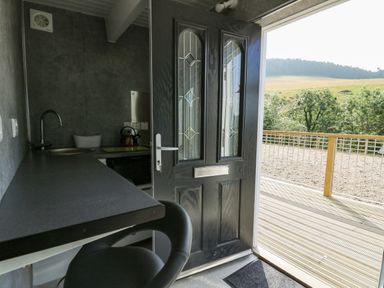 A small kitchen area with a black door open to a wooden deck and countryside view at Caban Glas in Llanafan near Pontrhydfendigaid