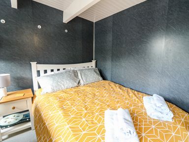 A bedroom with a bed with yellow patterned bedding beside a wooden nightstand with a lamp at Caban Glas Llanafan near Pontrhydfendigaid