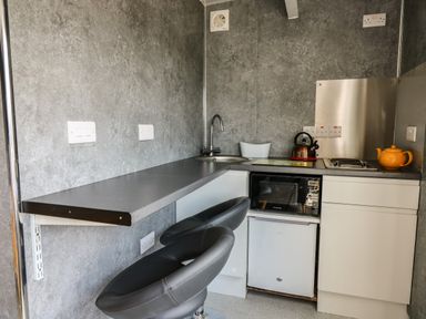 A small kitchen with a countertop and two black stools a sink a microwave a mini fridge a kettle and a teapot at Caban Glas in Llanafan near Pontrhydfendigaid
