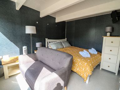 A bedroom with a bed with yellow geometric bedding a gray sofa two lamps a white dresser and dark walls at Caban Glas Llanafan near Pontrhydfendigaid